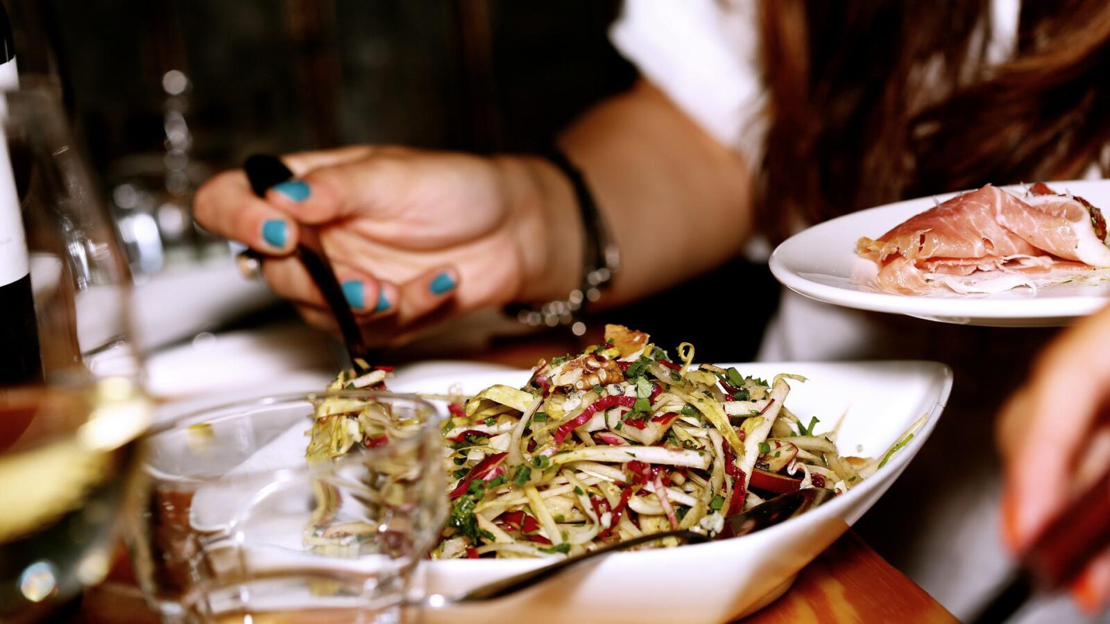 hand with blue nail varnish holds a fork above a bowl of delicious salad